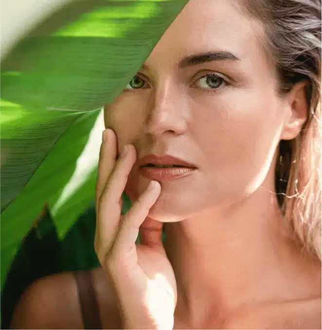A woman poses elegantly against a backdrop of a green leaf, emphasizing a serene and natural environment.